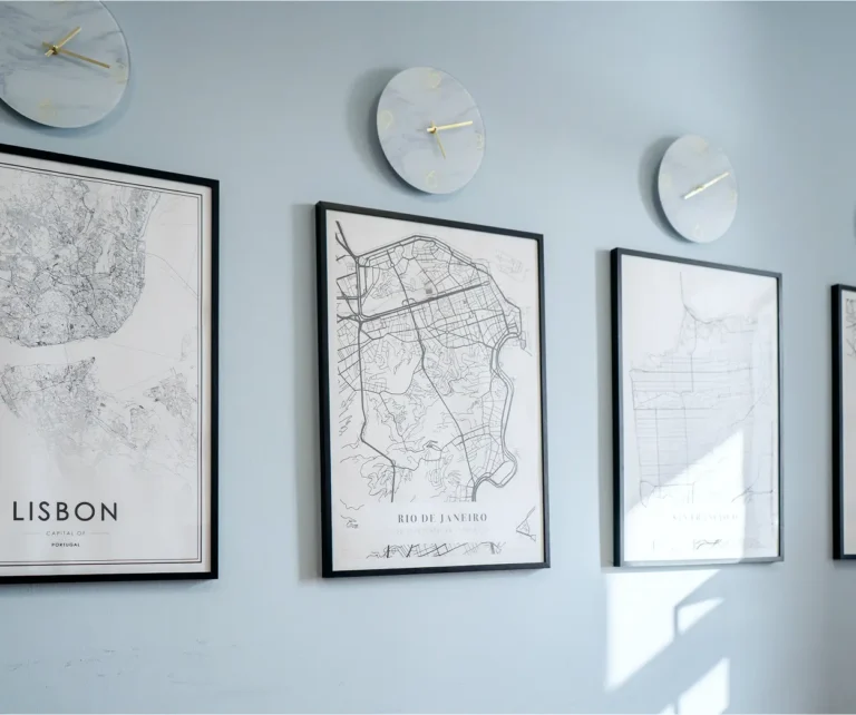 Three clocks and framed city maps on a pale blue wall.